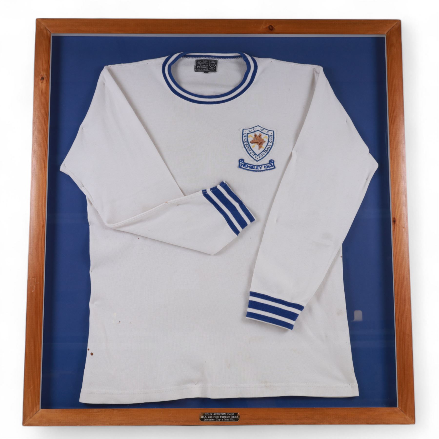 F.A. Cup Final Wembley 1963 Leicester City V Manchester United match worn long sleeved shirt, worn by Colin Appleton Leicester City captain, all white with striped blue collar and cuffs, embroidered cloth Leicester City badge with Wembley 1963 below, with Bukta Dyfast Zeebux label to inner collar, contained within a glazed wooden display frame with engraved plaque reading Colin Appleton (Capt) F.A. Cup Final Wembley 1963 Leicester City V Man Utd, frame H80cm

Notes: The 1963 F.A. Cup final was played on 25 May 1963 at Wembley 'Empire' Stadium. The final was won by Manchester United 3-1. 

Colin Harry Appleton (7 March 1936 – 31 May 2021) was an English footballer and manager. He captained Leicester during their 1962-63 season and the FA Cup final of this year. He then went on to captain them to the 1964 League Cup win. 

He later played for Charlton Athletic and Barrow, before playing for and managing Scarborough. He went on to manage Hull City, Swansea City, Exeter City and Bridlington Town.