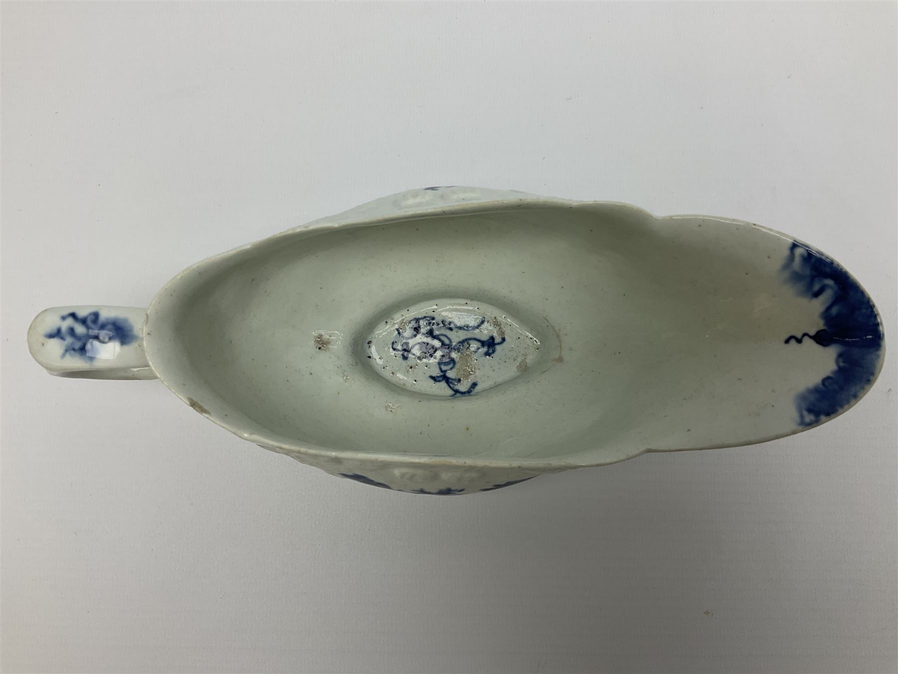 Large 18th century Lowestoft sauce boat, circa 1770, the body decorated with Hughes type floral moulding, and painted in underglaze blue with an Oriental landscape, and foliate sprigs, L23cm