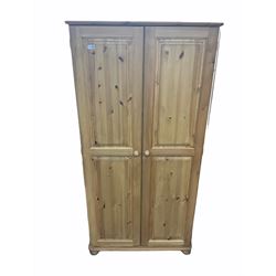 Solid pine double wardrobe, two panelled cupboard doors enclosing hanging rail, raised on bun feet 