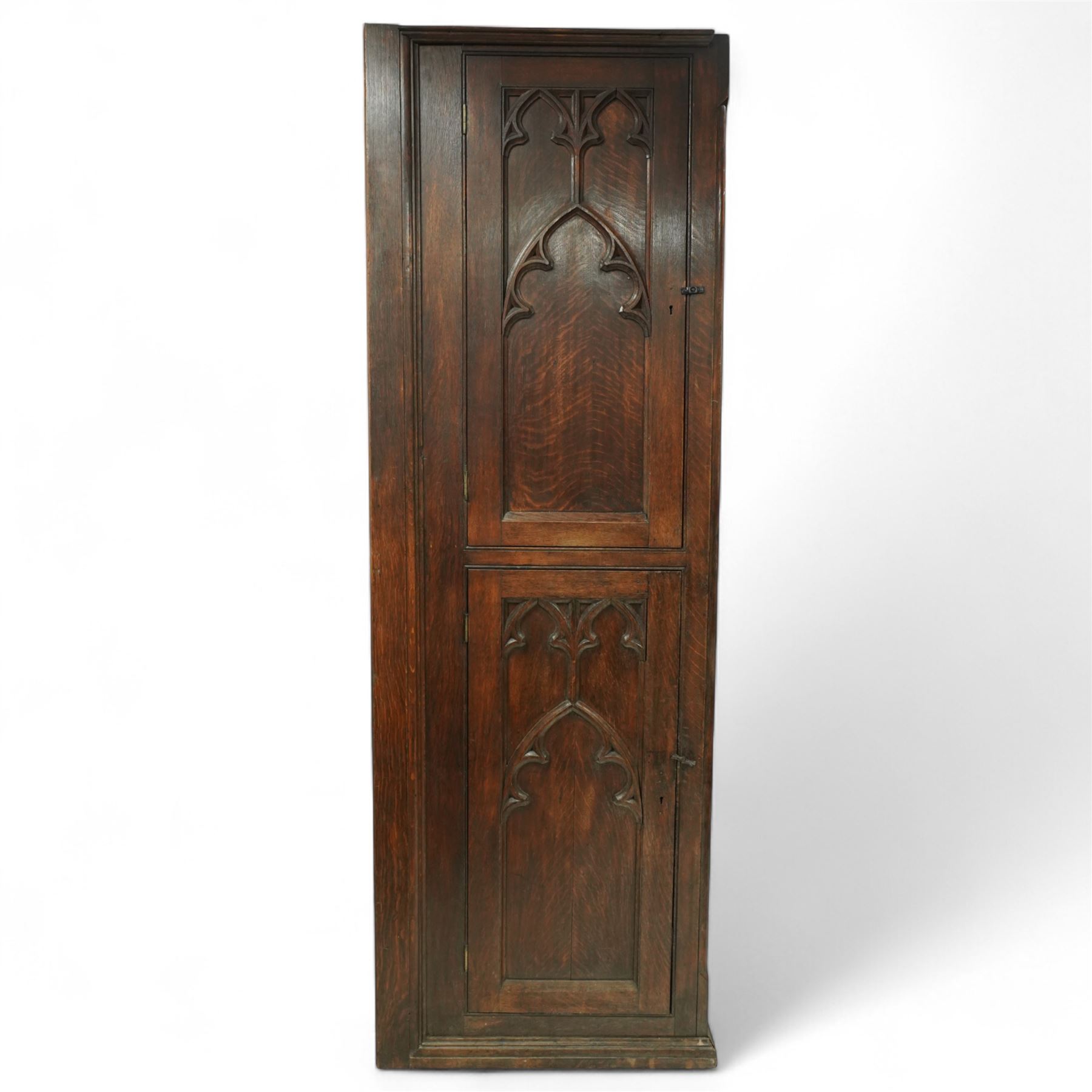 19th century Gothic Revival oak Sacristy vestment cupboard of tall proportions, fitted with two ecclesiastical trefoil moulded panelled doors enclosing four shelves, flanked by a chamfered corner, the side panelled and moulded with matching sacristic architectural mouldings, on skirted base