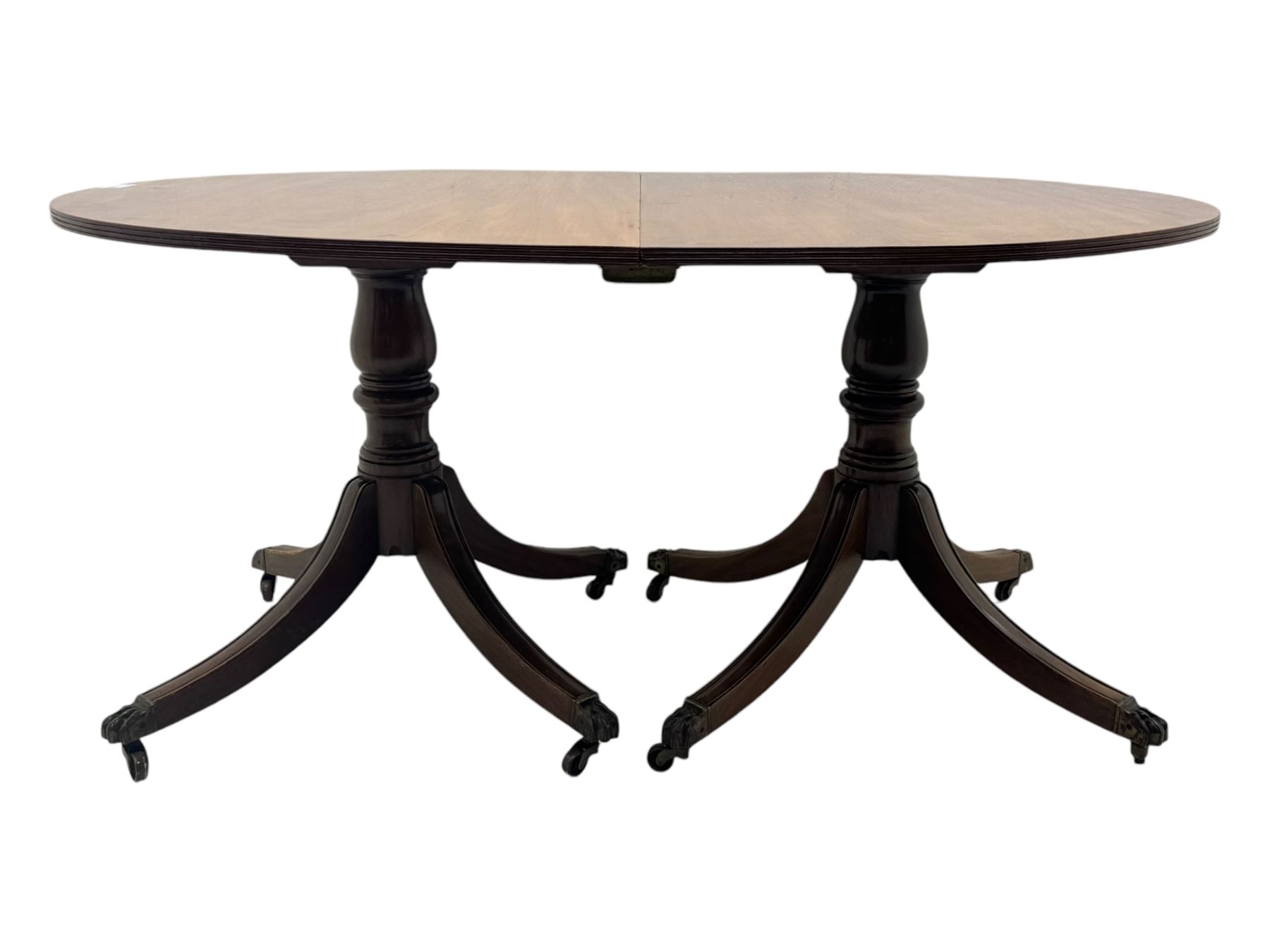 Georgian design mahogany twin pedestal dining table, oval top with reeded edge, single additional leaf, on turned pedestal with four out splayed supports, cast brass hairy paw castors 