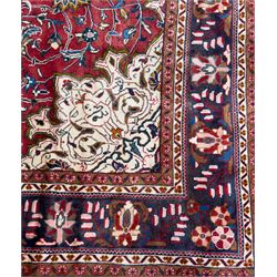 Northwestern Persian Lillihan hand-knotted carpet, madder red field with scrolling vines, rosettes, and palmettes around a central circular medallion in navy, ivory and ochre, and ivory ground spandrels within a navy border of stylized flowerheads and vines between multiple guard stripes 