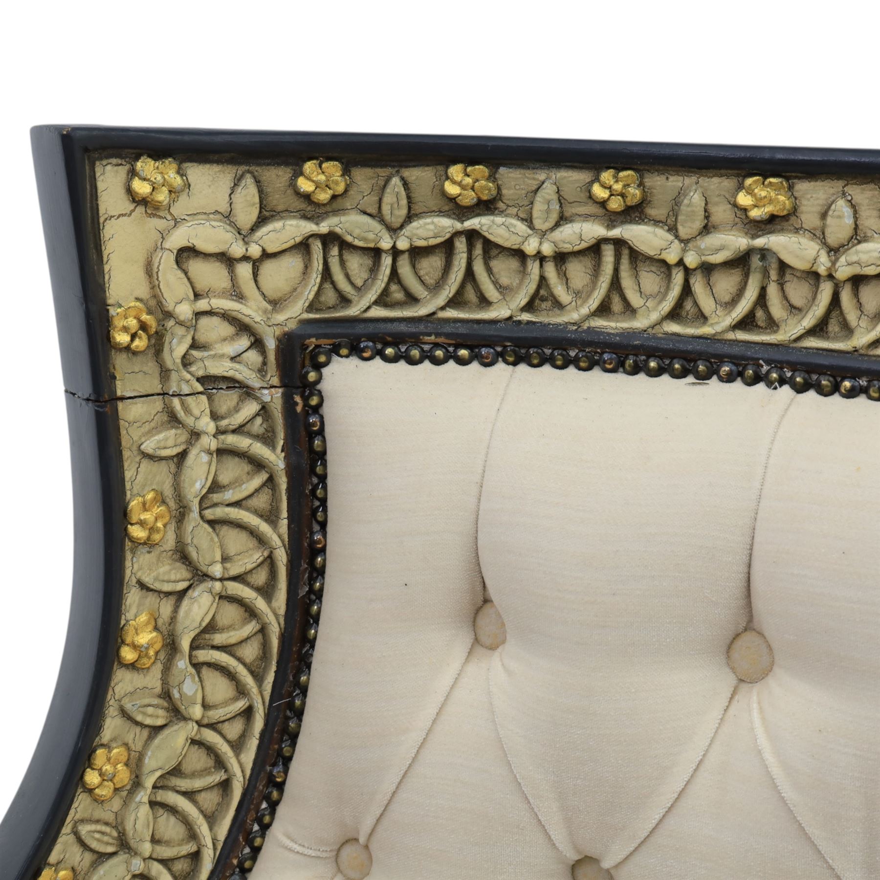 20th century Louis XVI style settee, upholstered in cream fabric with buttoned back and arms, and plain seat cushions, the shaped and black painted frame with entwined foliate detail and gilt flower heads, upon column legs with bun feet