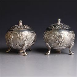 Pair of Middle Eastern silver cruets, of spherical form with pierced tops, embossed with figures, elephants and village scenes, unmarked, together with a pair of silver condiment spoons embossed with floral decoration 