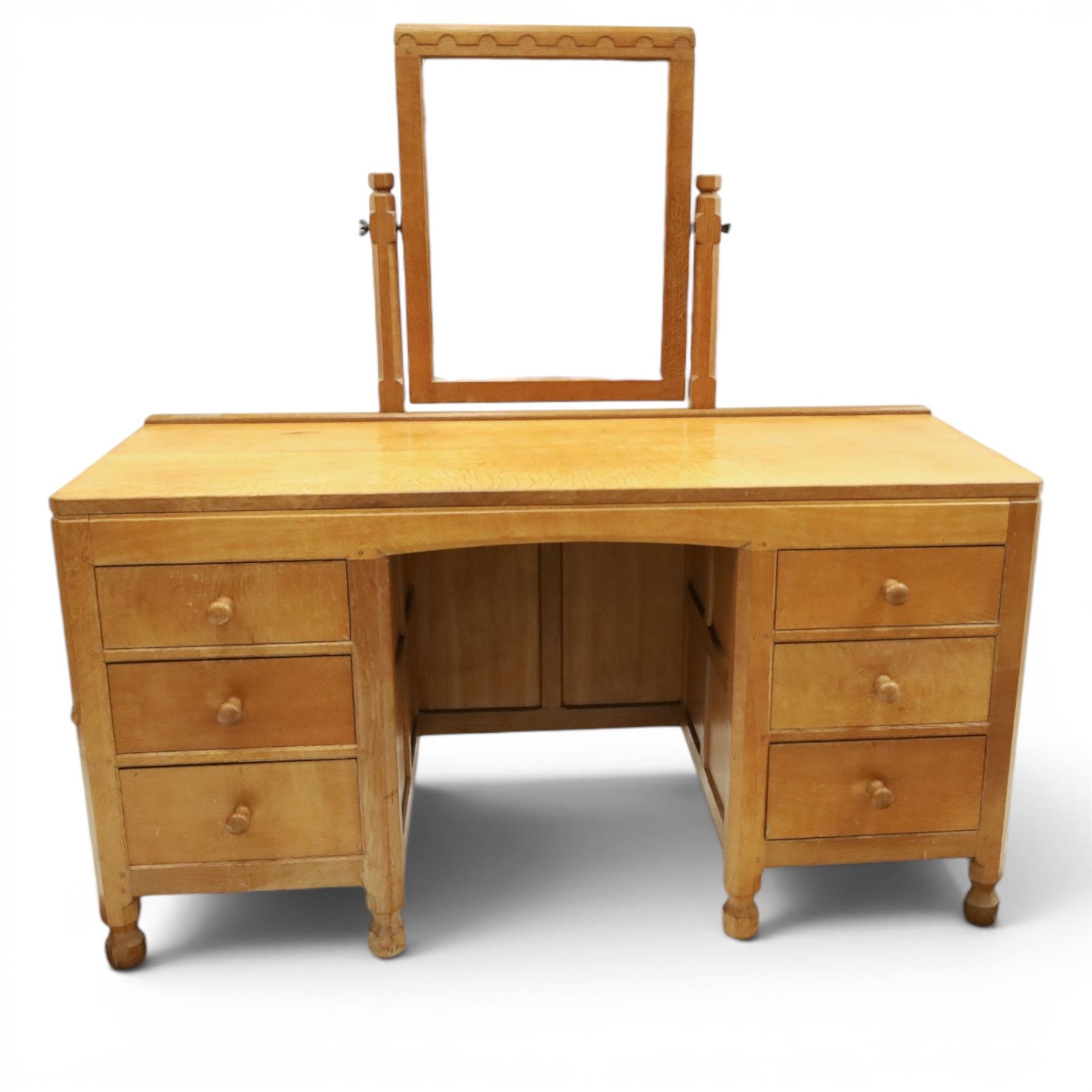 Mouseman - adzed oak kneehole dressing table with mirror, the rectangular adzed top with raised back and canted corners with fixed central pivoting mirror with scallop-carved cresting rail, over an arched recessed kneehole flanked by three graduating drawers to each side with turned knob handles, raised on octagonal feet, with carved mouse signature, by the workshop of Robert Thompson of Kilburn