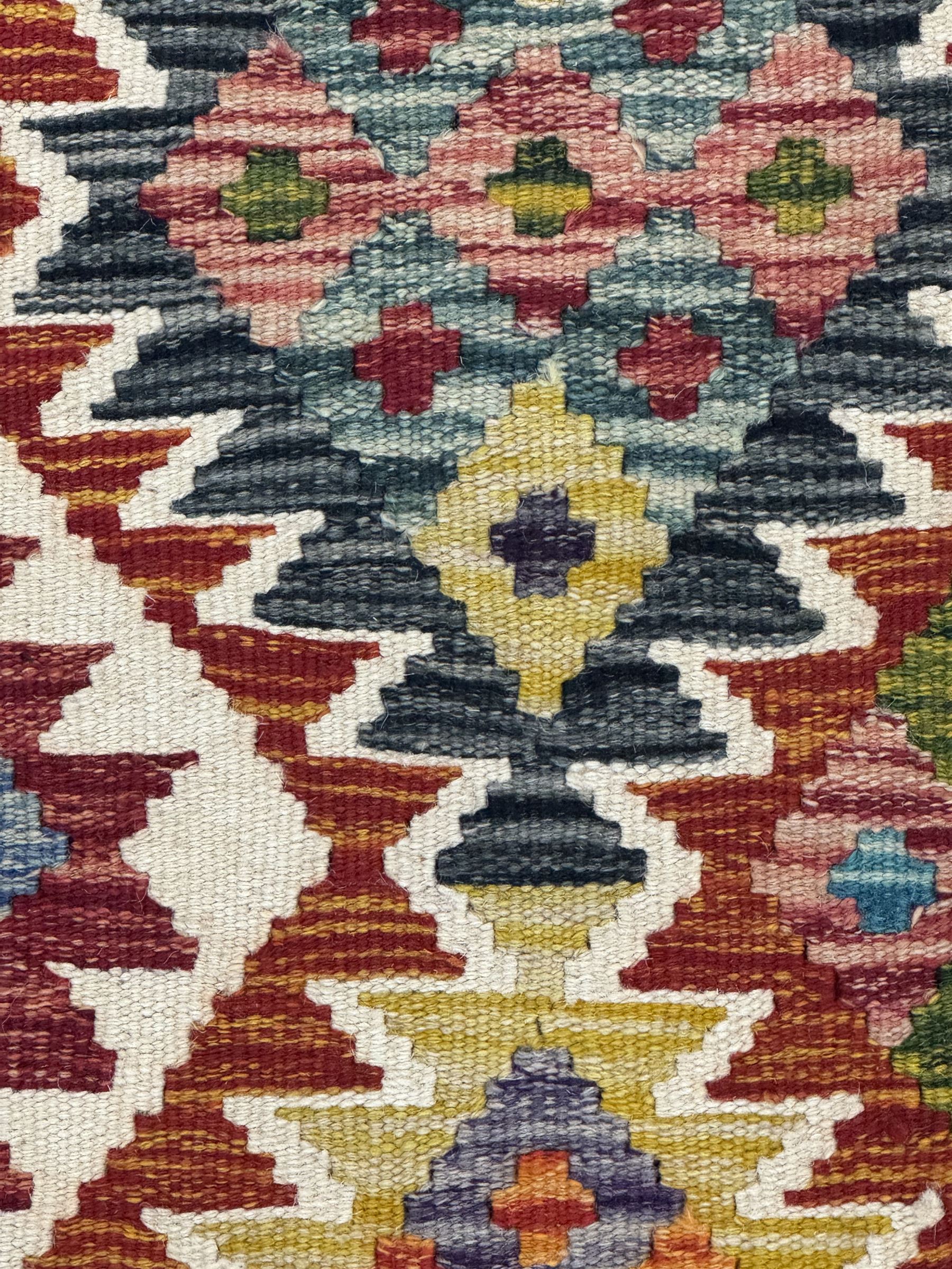 Chobi Kilim flatweave rug, cream ground with a multicoloured geometric diamond field, framed by a bold border of repeating stylised motifs, finished with braided corner tassels