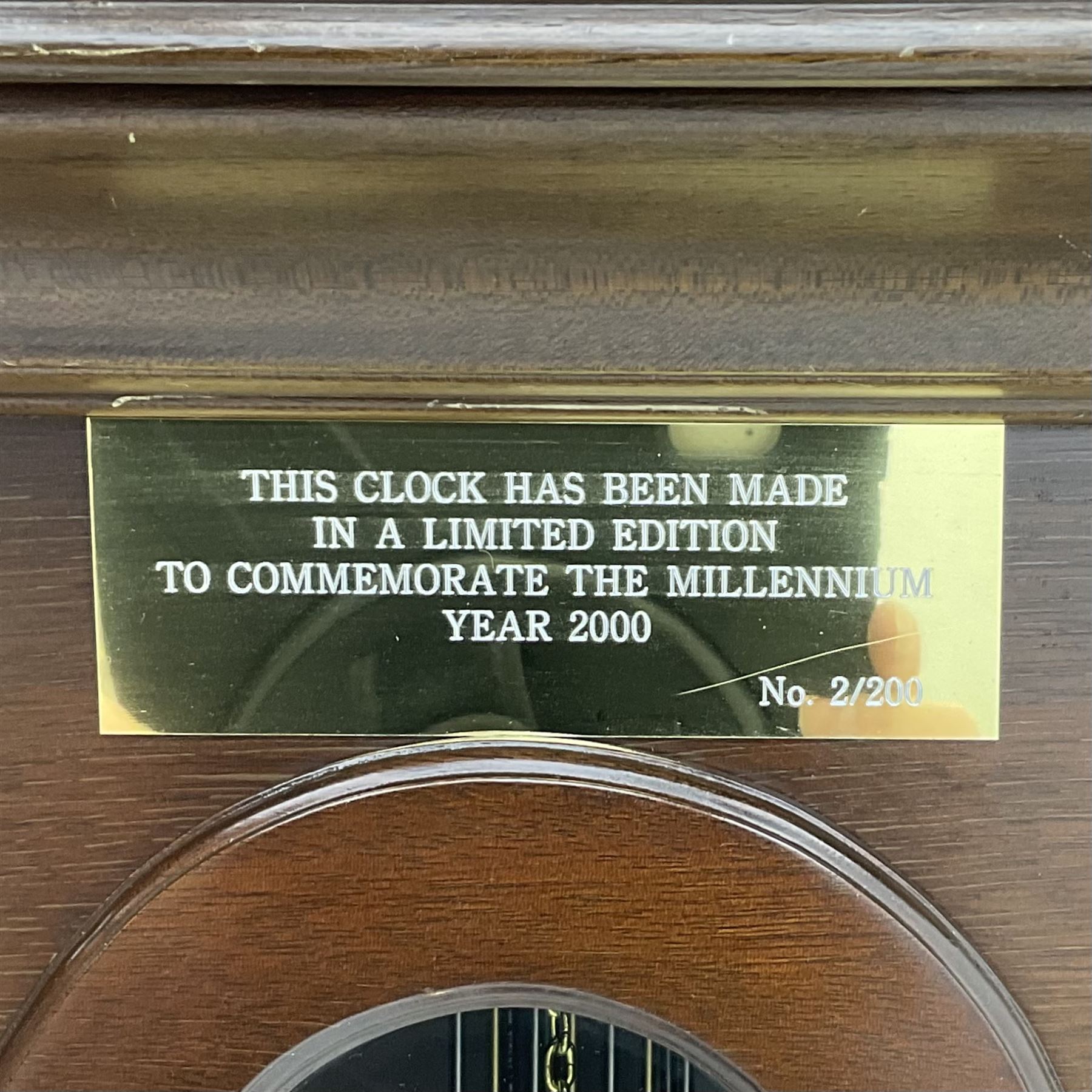 A  20th century longcase clock made to celebrate the millennium in the year 2000, this clock being No 2 of only 200 manufactured by  Richard Broad in Bodmin Cornwall, with a mahogany effect case and traditional swans neck pediment with three brass finials, break arch hood door on a trunk with recessed columns and full length glazed door, on a square plinth with inlay and a shaped base, brass dial with brass spandrels, silvered chapter ring, seconds dial and working moon phase to the arch, weight driven three train movement striking the quarters and hours on 12 gong rods, with a choice of St Michael, Westminster and Wittington chimes, with chime selector and chime/silent facility. With three brass cased weights and gridiron pendulum.





