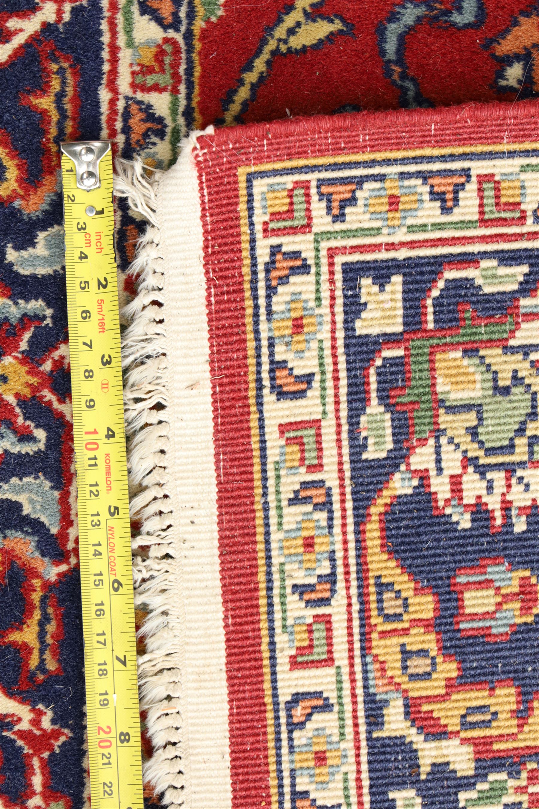 Persian Kashan crimson ground rug decorated with scrolling foliage, the indigo guard stripes with repeating stylised palmette motifs
