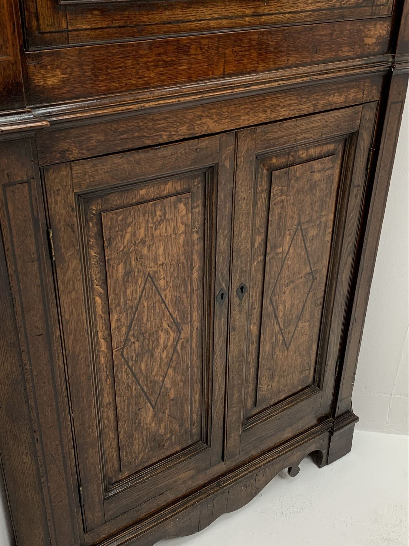 George III oak floor standing corner cabinet, scrolled swan neck pediment with central finial over astragal glazed door, painted interior fitted with three shaped shelves, the lower section fitted with single shaped shelf enclosed by two fielded panel doors inlaid lozenges, on bracket feet, H195cm, W77cm