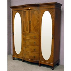  Edwardian triple mahogany wardrobe, projecting cornice above two bow fronted panelled doors with three adjustable shelves, four central graduating drawers, two full height doors with bevel edged oval mirrors, interior with hanging rails, hooks and drawer units, spade supports, W195cm, H219cm, D59cm  
