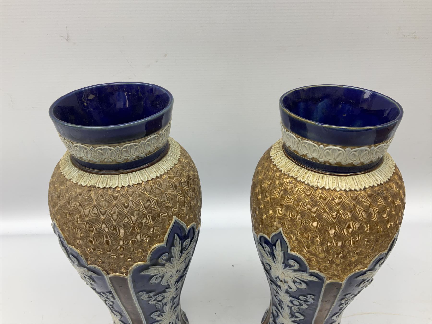 Pair of Royal Doulton Lambeth stoneware baluster vases, decorated in light relief with panels of foliage on blue ground, with gilt scrolls above, impressed mark beneath, 28cm high