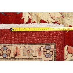 West Persian Sarough hand-knotted carpet, rich madder red field, decorated with stylized palmettes angular vinery and floral sprays within multiple borders of ivory ground and scrolling foliate decoration, with cotton fringe ends 