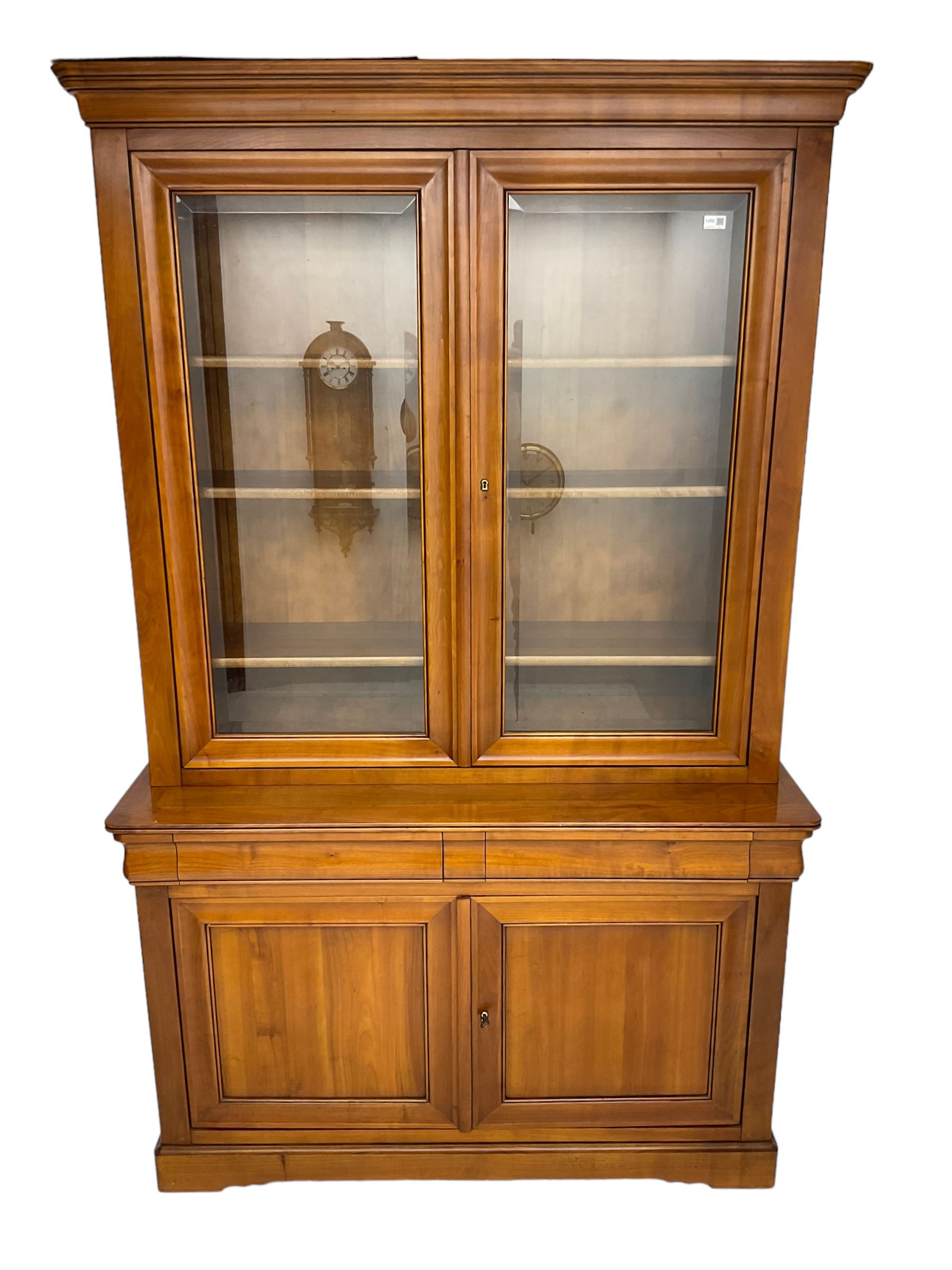 French cherry wood bookcase on cupboard, projecting cornice over two cupboard doors with bevelled glass panels enclosing three adjustable shelves, base fitted with two cushion drawers over double cupboard