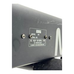 Korg M1 keyboard synthesiser, 61 velocity-sensitive keys with integrated multi-effects and eight-track sequencer, mounted on an adjustable black tubular X-frame stand with rubber end caps