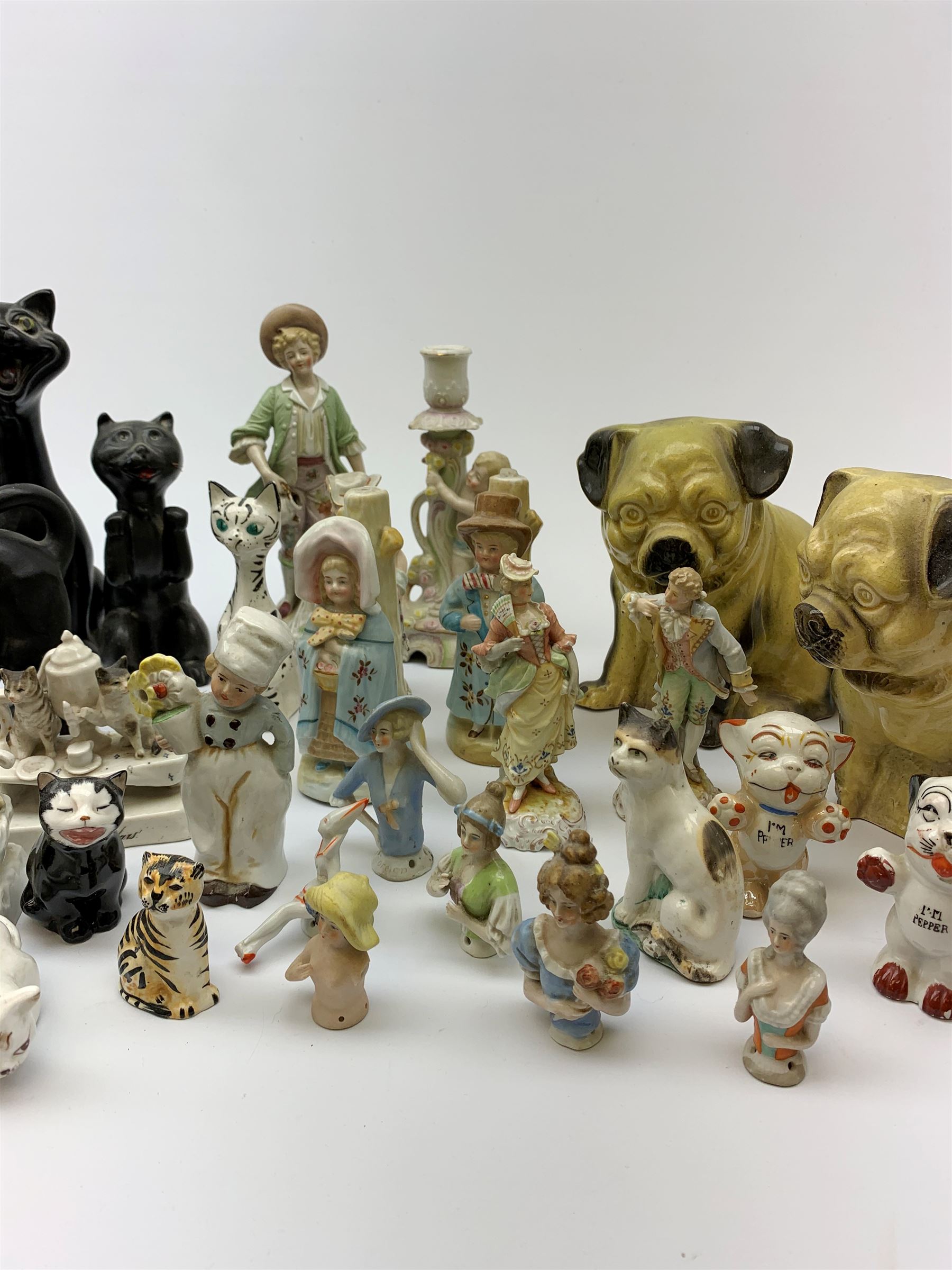 A collection of various ceramic figurines, to include pair of small 19th century Staffordshire cats, Royal Doulton cat, Coalport cat, pair of 19th century pug dogs, two fairings inscribed Good Templars, two Bonzo dog peppers, a number of pin cushion dolls, various 20th century and later black pottery cats, Victorian bisque figures, etc. 