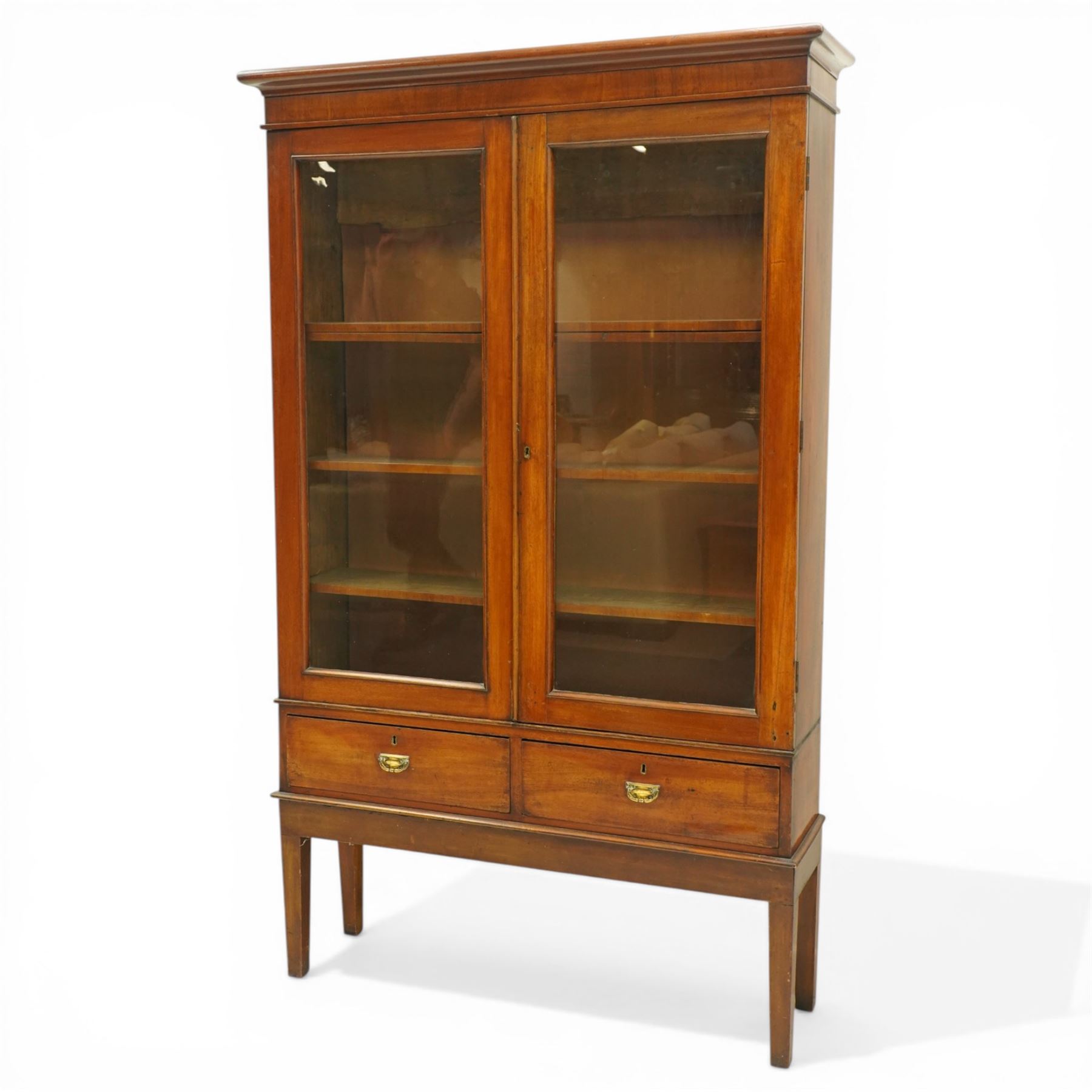 19th century mahogany enclosed bookcase on stand, projecting cornice and banded frieze over two glazed doors enclosing four adjustable shelves, fitted with two drawers to base, on square tapering supports