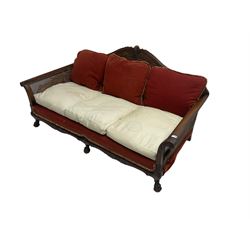 Early 20th century bergère three seat settee, shaped shell carved cresting rail, double caned back and sides, scrolled upright arms and shaped apron carved with shell and foliage, on hairy paw carved feet