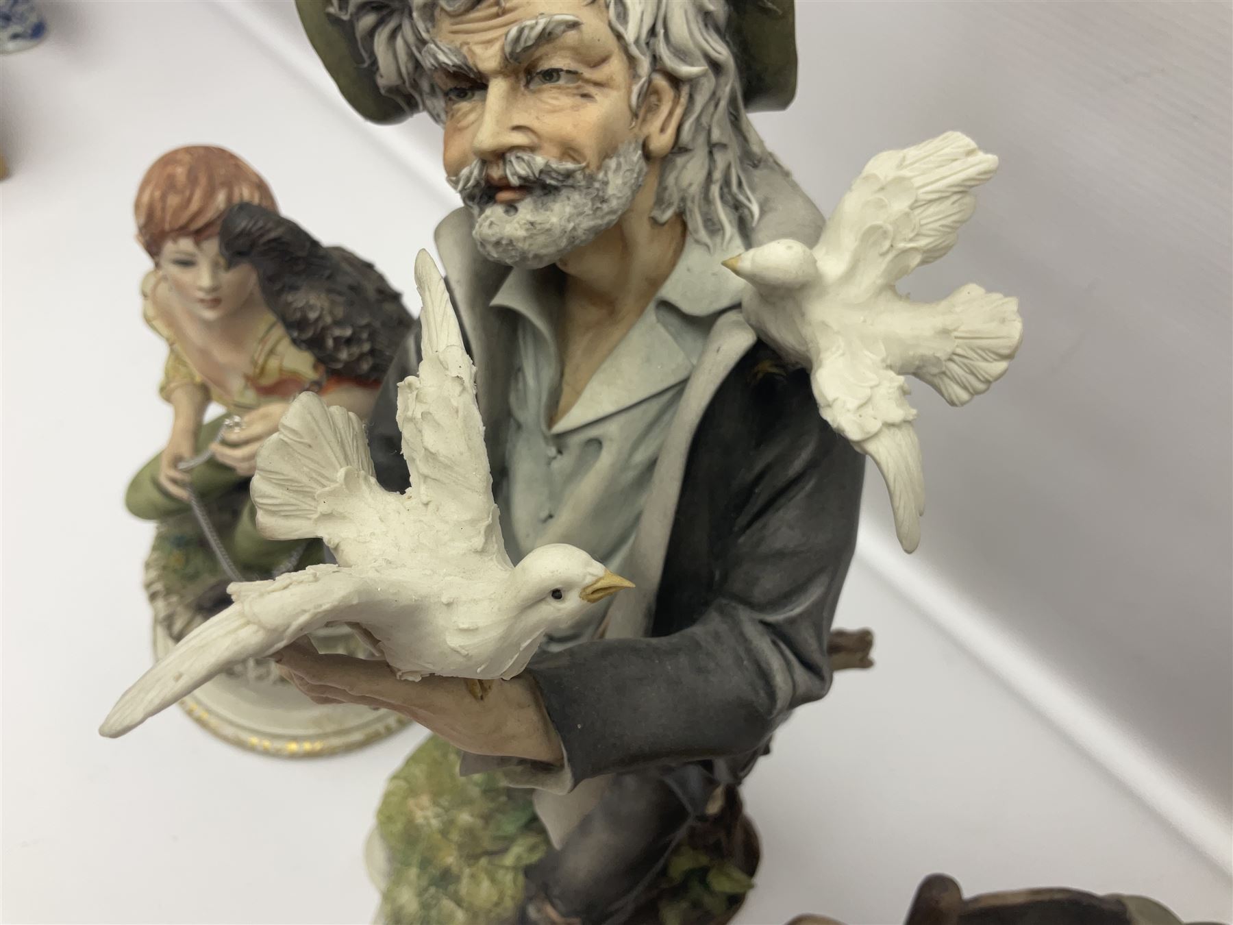 Three Capodimonte figures, to include The Kind Heart Man, modelled by Cortese as a tramp with two doves, The Young Falconer by Maria Angela and another modelled as a tramp darning his socks, all with printed marks, tallest H39cm