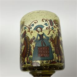 19th Century Bohemian amethyst glass lidded goblet, the bowl of faceted form, gilded with three children in period dress playing games, upon a knopped stem and conforming faceted foot, together with an art nouveau green glass goblet, with gilded rim, upon clear trumpet stem, and a hand blown wine glass, transfer printed with birds and three figures in period dress, tallest H29cm