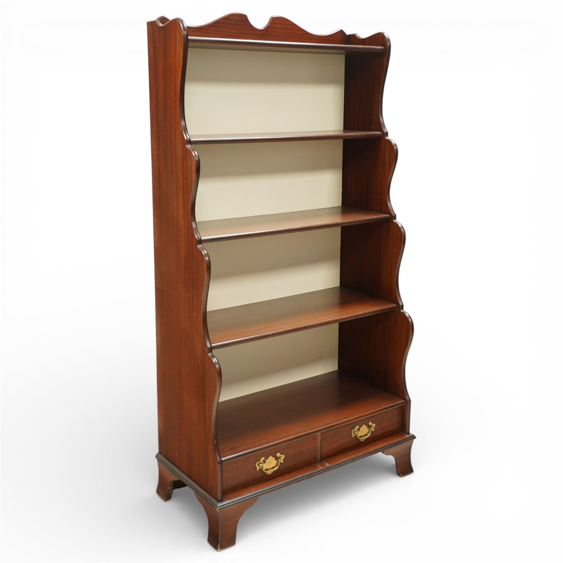Early 20th century mahogany waterfall bookcase, shaped and serpentine side uprights with scalloped cresting, fitted with four open shelves above two short drawers with brass drop handles, raised on shaped bracket feet