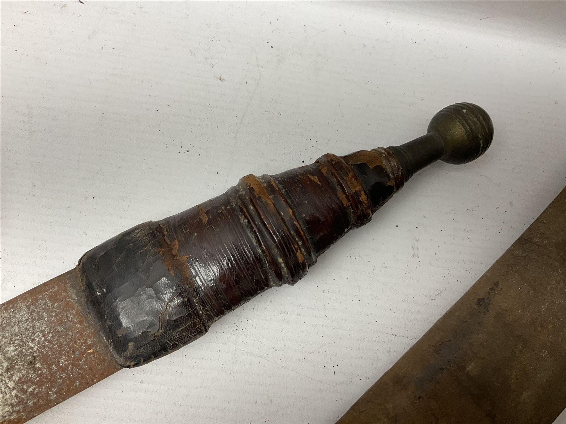 Mandingo sword, the 63cm plain curving steel blade marked with a horses head and the initials G.S.; leather covered grip with metal ribbed spherical pommel; in decorative leather leaf scabbard mounted with tassels and roundels L84cm overall; and a North African flyssa sword in poor condition with wooden scabbard (2)