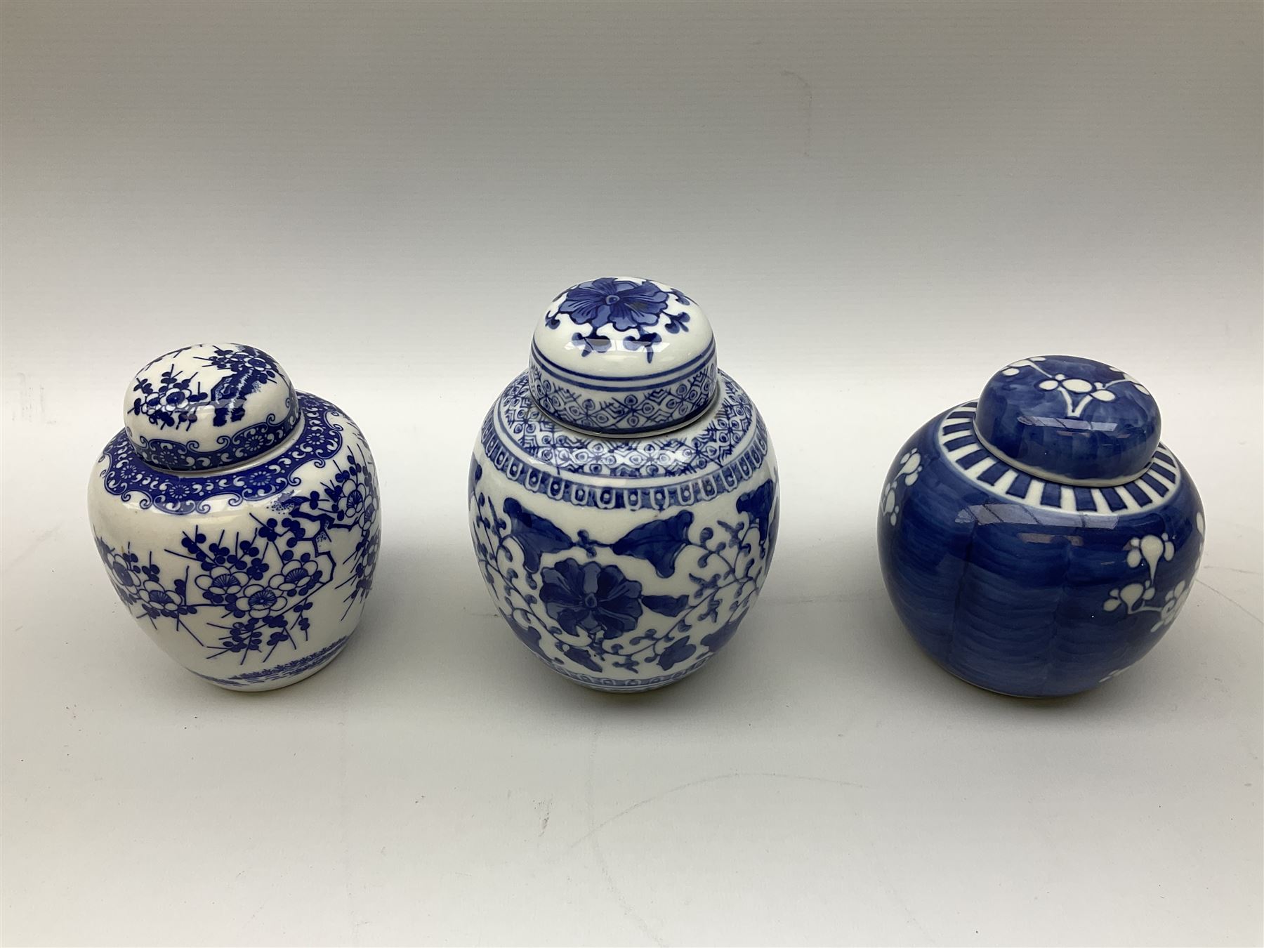 Six Chinese ginger jars, predominantly of blue and white design decorated with blossoming branches, all with lids, housed on various hardwood carved stands, some with character marks beneath