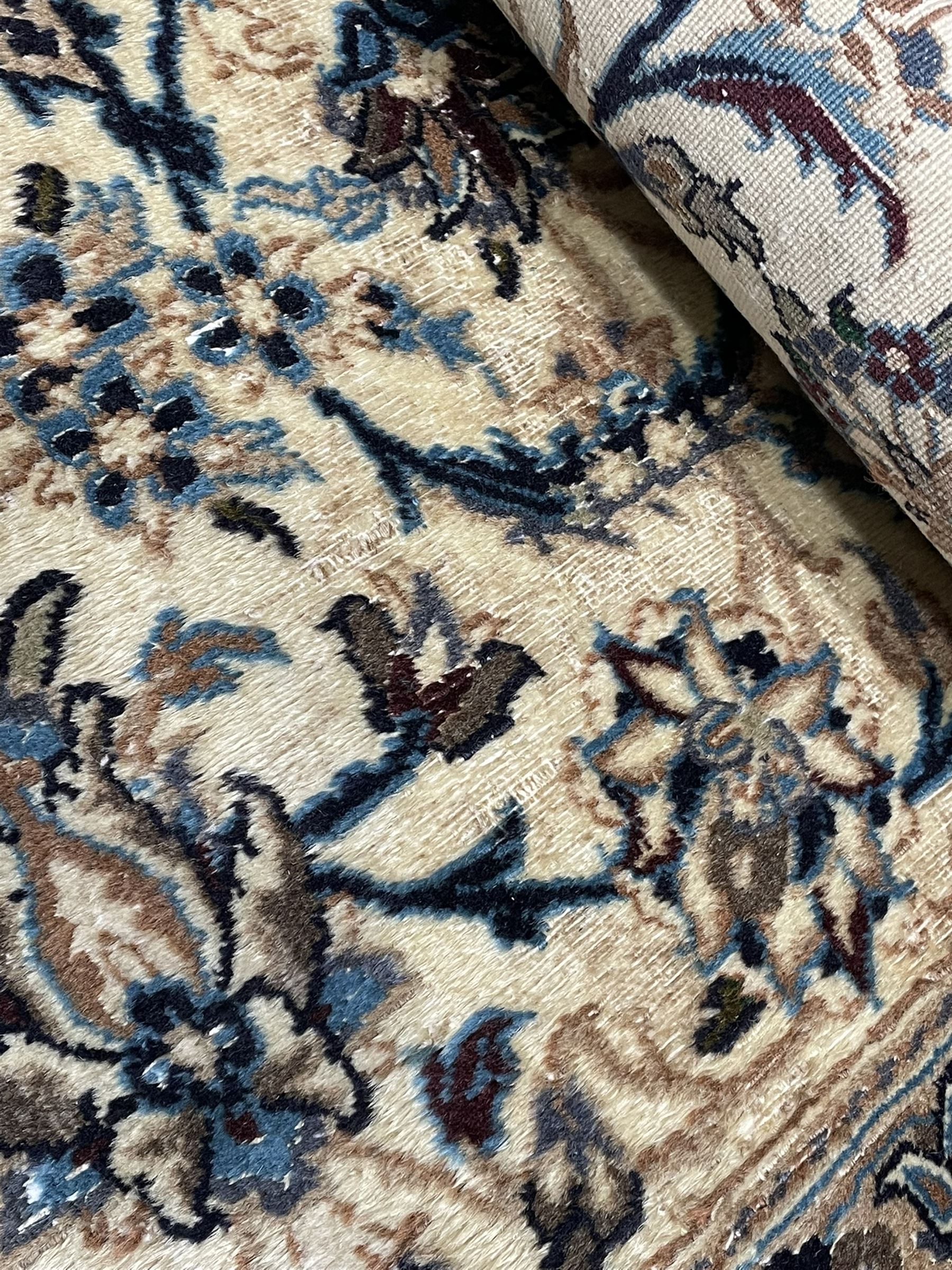 Persian Kashan ivory ground carpet, central rosette medallion surrounded by swirling leafy branches and floral sprays, the main border with scrolling pattern interspersed with floral motifs, within guard stripes 