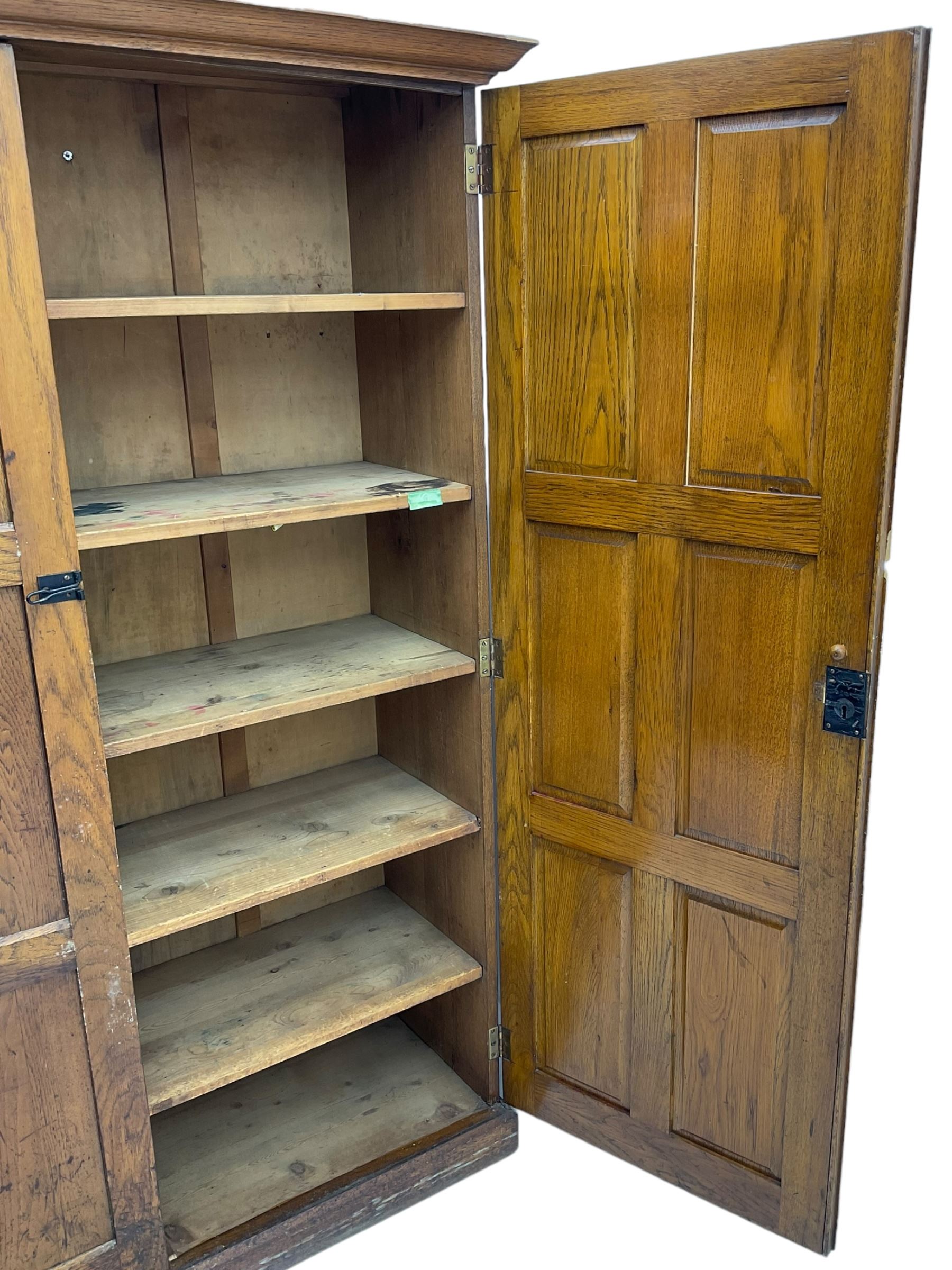 The North of England School Furnishing Company Limited Darlington - early 20th century oak school cupboard, projecting moulded cornice over two panelled doors, fitted with shelves, on chamfered plinth base 