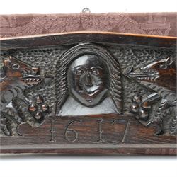 17th century walnut frieze, or pediment, carved with a smiling mans faced flanked my two creatures, incised date 1617, mounted on fabric panel, W52cm