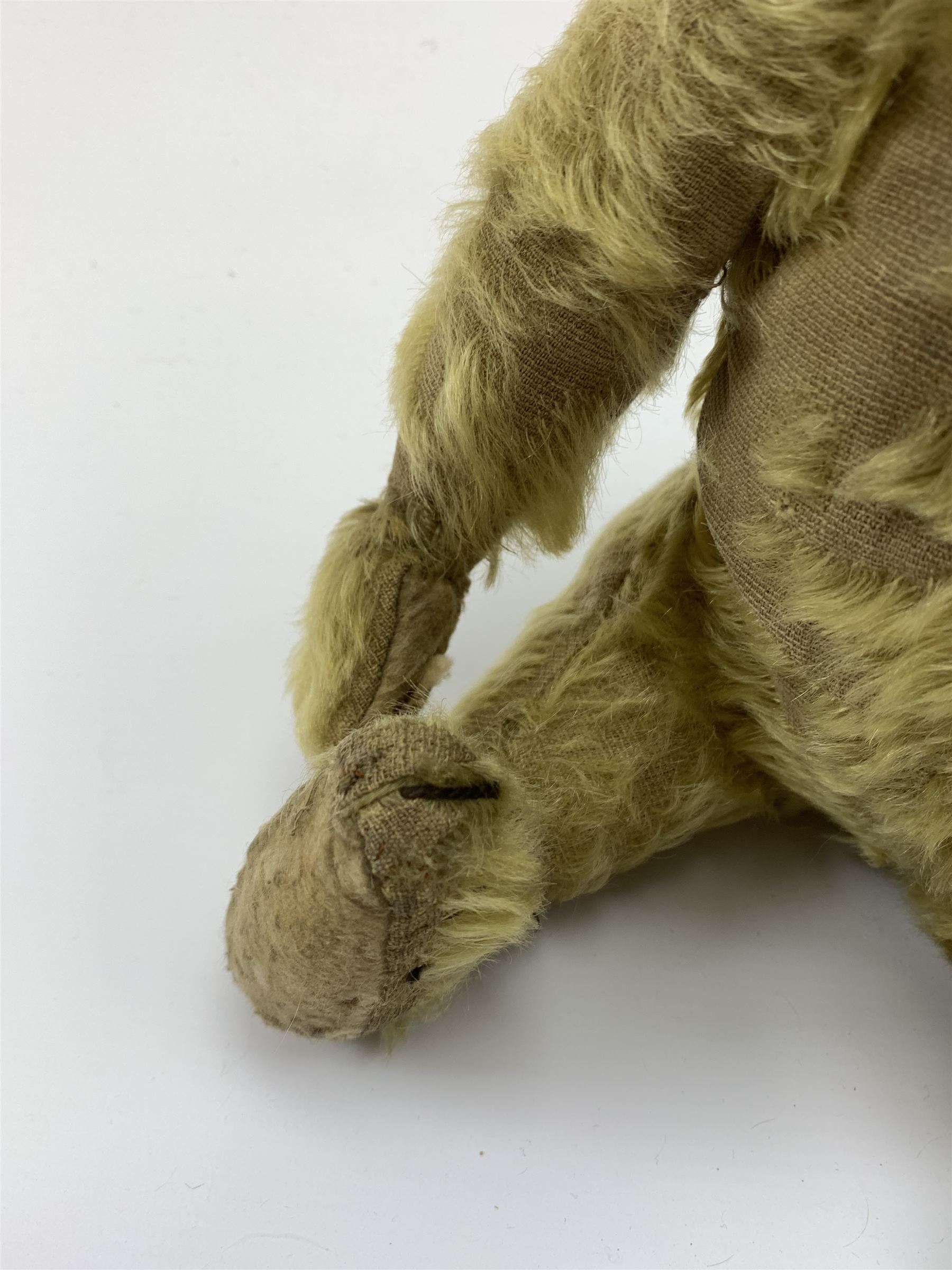 Early 20th century English teddy bear, with wood wool filled body with jointed limbs, felt covered paw pads, five claw stitching to feet and elongated arms with spoon shaped paws H14