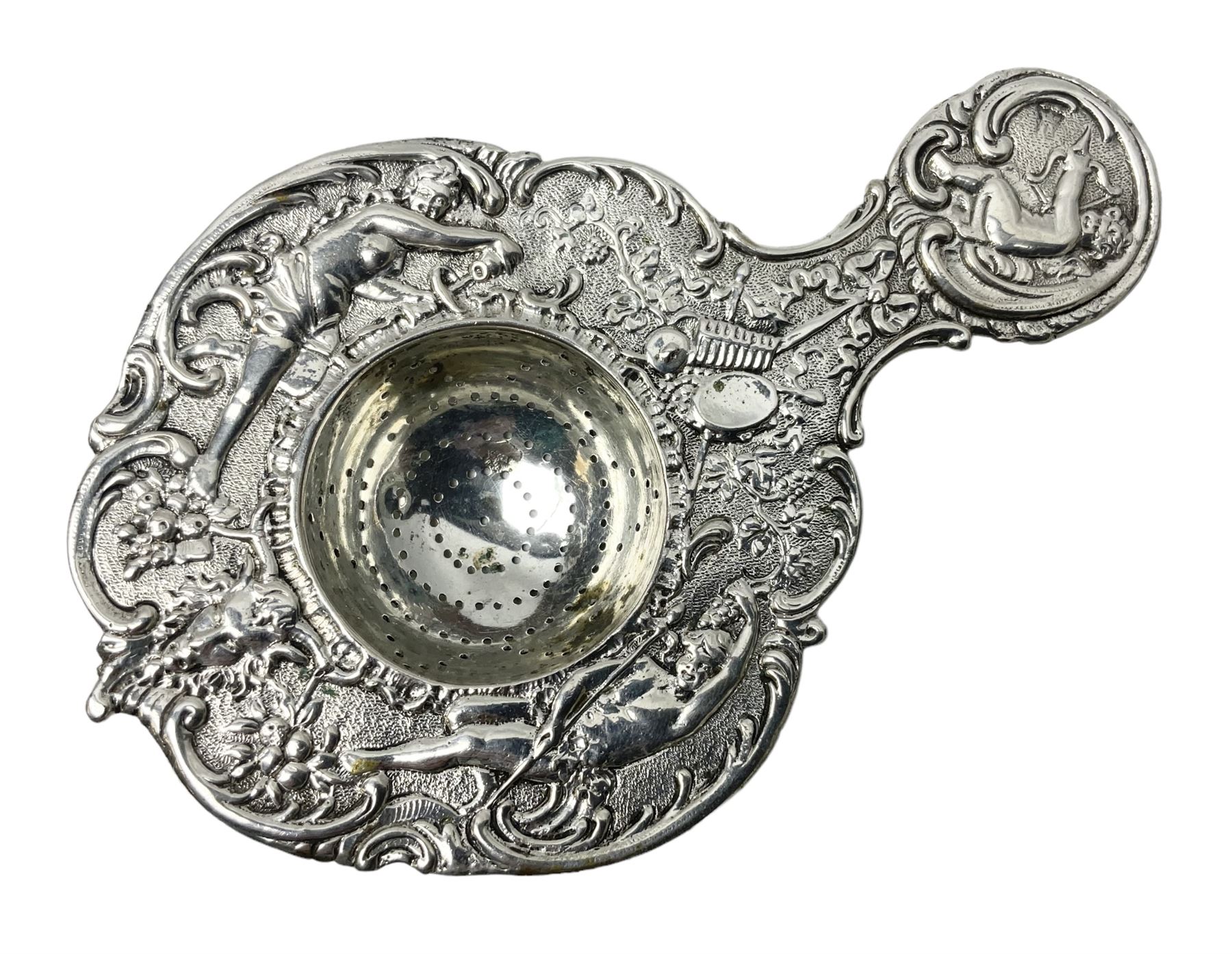 Continental white metal strainer, of shaped form embossed with classical figures, putto, musical trophies and fruiting vines, indistinctly marked, L12.5cm