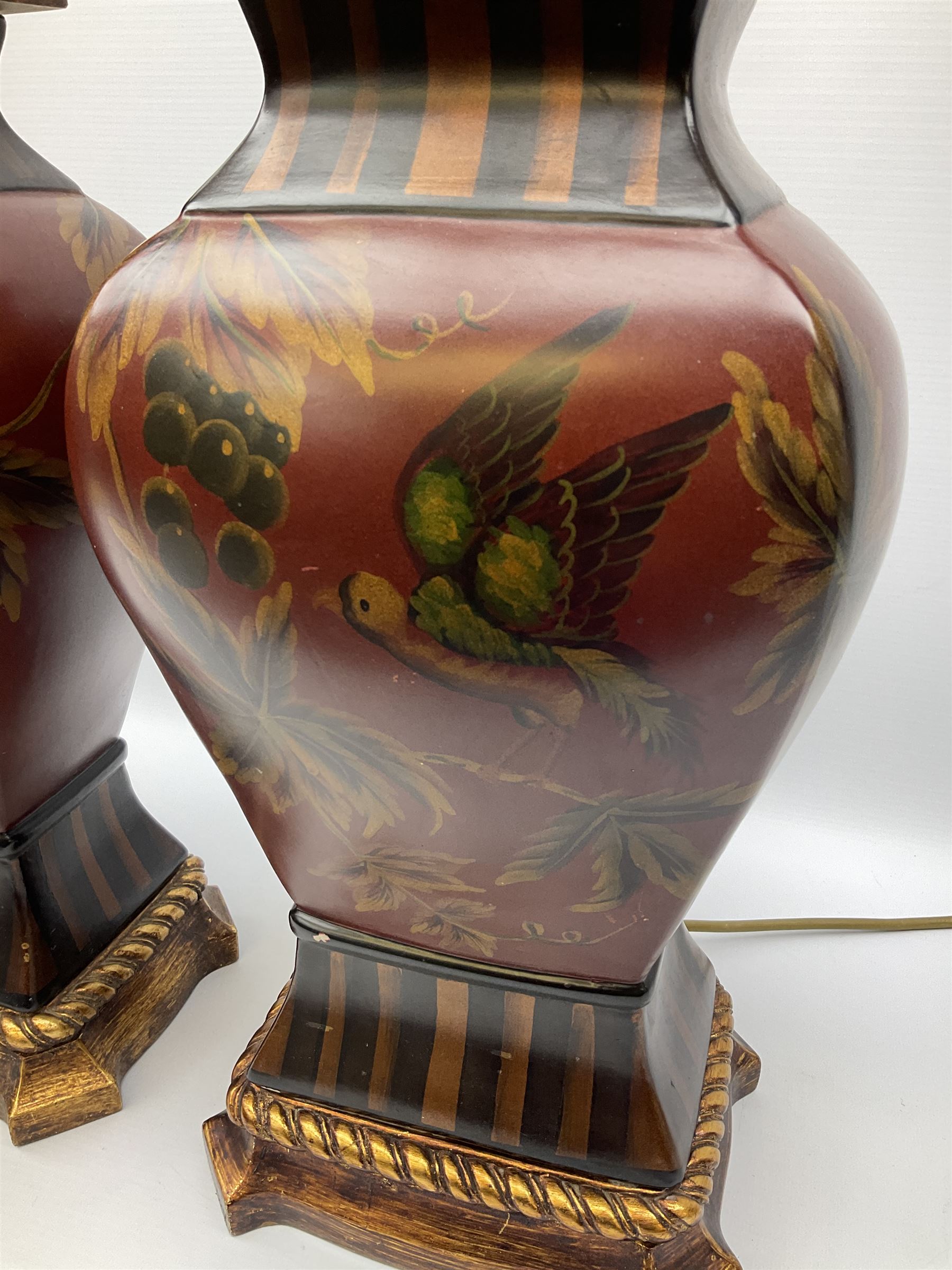 Pair Oriental table lamps decorated with birds in a tree with fruit, on a red ground with a gilded base together with cream lampshades H57cm, without lampshade. 