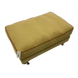 Rectangular footstool, upholstered in pale yellow fabric with peach piping, on mahogany finish feet with brass castors