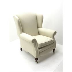 Georgian style high wing back armchair, upholstered in cream fabric, turned supports on castors