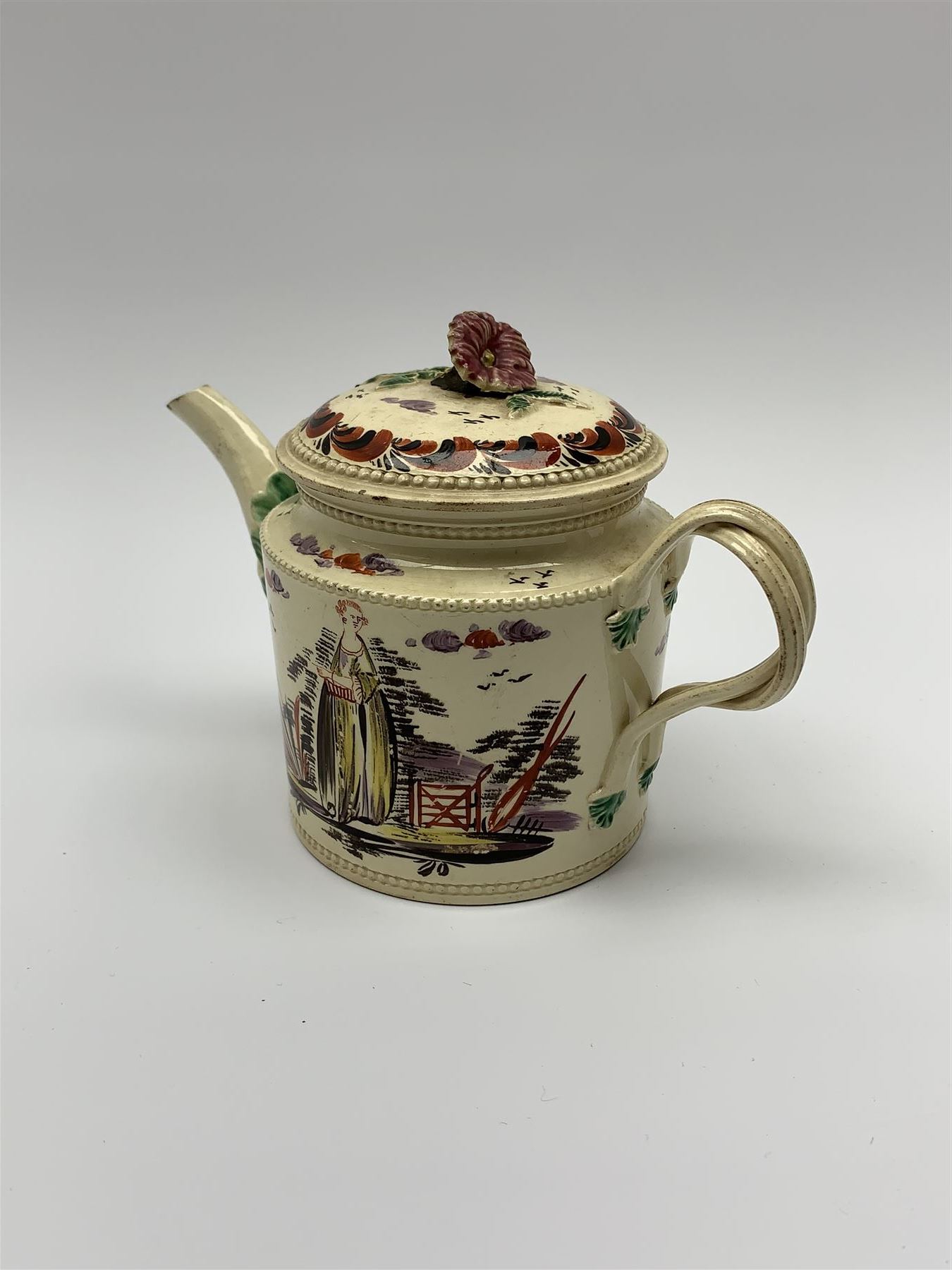 18th century creamware teapot, probably Leeds, with reeded entwined handle and floral finial to the cover, the body with hand painted polychrome decoration of figure to one side, and floral spray to the other, collectors paper label beneath inscribed Leeds Pottery, H11.5cm