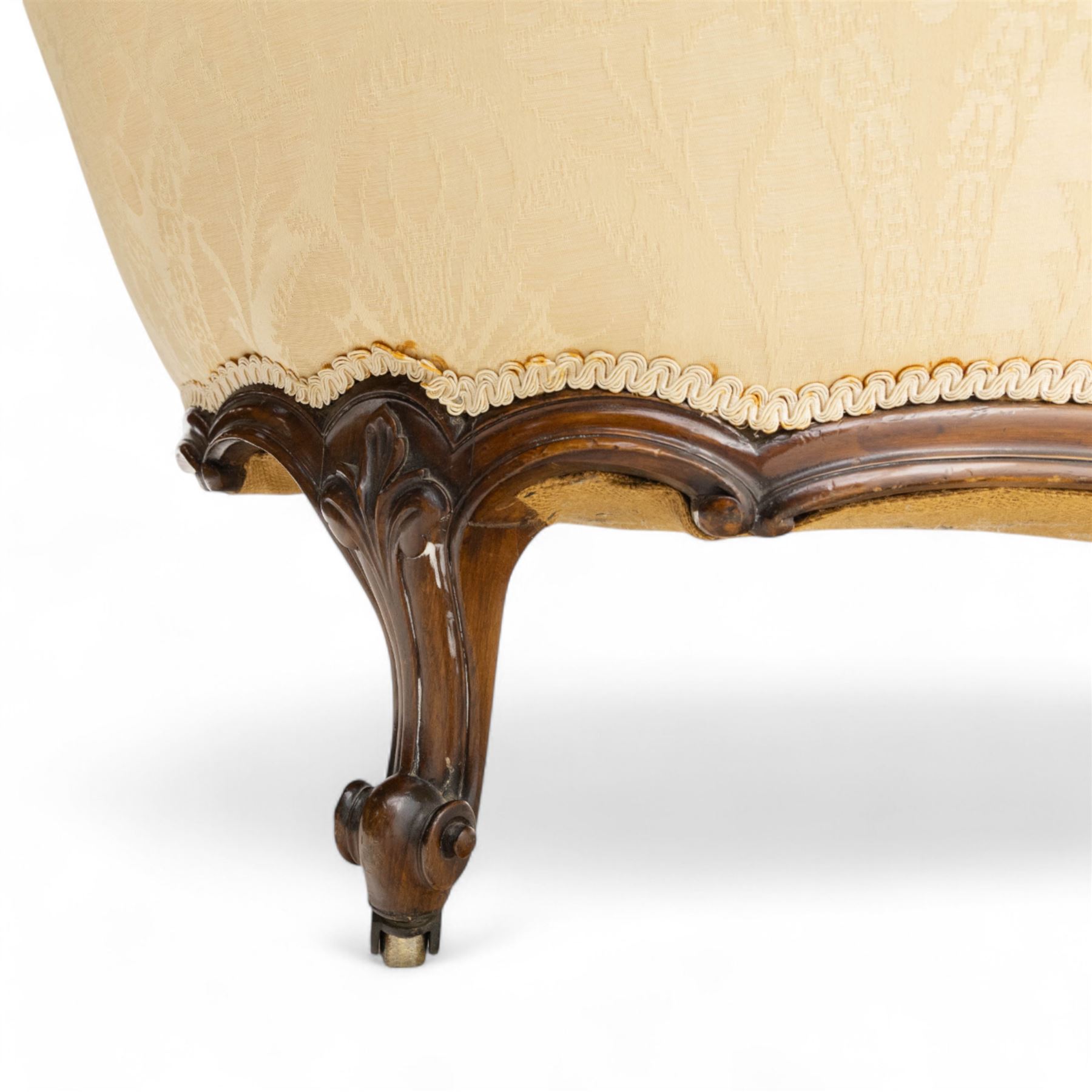 Late 19th century Victorian walnut button-back recamier, asymmetrical form, with cream damask fabric and gimp braid edging, shaped reeded apron above front and back scroll carved cabriole legs on brass castors