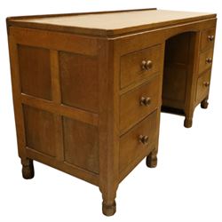 Mouseman - adzed oak kneehole dressing table or desk, the rectangular adzed top with raised back and canted corners, over an arched recessed kneehole flanked by three graduating drawers to each side with turned knob handles, raised on octagonal feet, with carved mouse signature, by the workshop of Robert Thompson of Kilburn