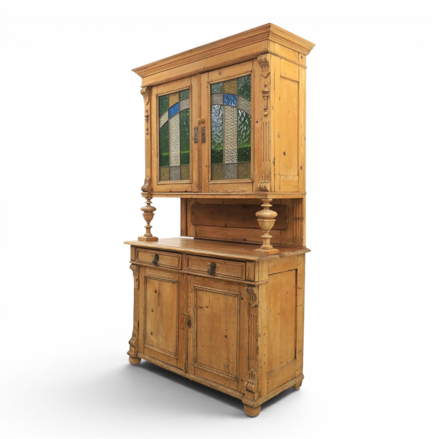 Late 19th century French pine dresser with stained glass upper section, the upper section with projecting cornice with fluted and scrolled details, enclosing a shelved interior, supported on turned front uprights, the lower section with frieze drawers and cupboard doors, raised on bun feet