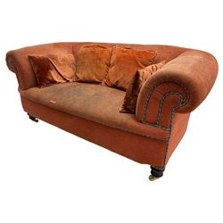 Late Victorian two-seat sofa, traditionally shaped with rolled arms, upholstered in rust fabric with blue and green entwined piping, together with scatter cushions, on turned front feet with brass and ceramic castors