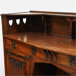 Shapland and Petter - Arts and crafts oak sideboard, rectangular overhanging top with raised open back fitted with shaped supports and pierced heart cut-outs to the ends, the base fitted with a central arrangement of two short drawers with cast metal drop handles over an open kneehole recess, flanked by a pair of cupboard doors each with linenfold panels and applied strap hinges, enclosing shelved interiors, raised on shaped bracket feet