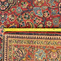 Persian Sarouk rug, richly decorated with an elaborate central medallion of palmettes and stylized floral motifs in indigo, ivory, and pastel tones on madder red ground, framed by spandrels, with a broad border of flowering palmettes and serrated leaves between a narrow floral guard border, fringe removed 