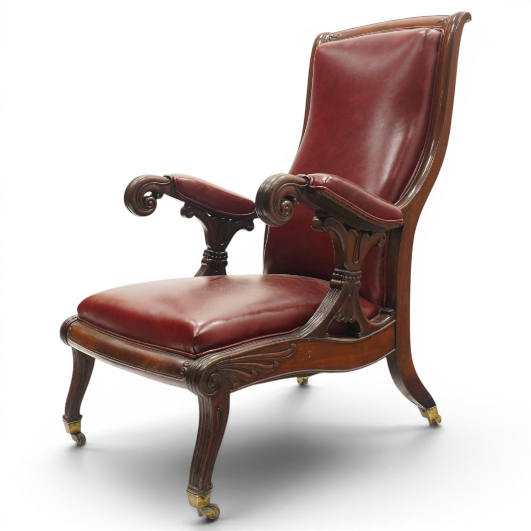 William IV mahogany high-back library reading armchair, arched cresting rail with moulded C-scrolls and bellflowers, the padded arms raised on waisted supports with lappet style carving below scrolled arm terminals, the lower reeded frame raised on splayed supports with brass cups and castors, upholstered in red leather with sprung seat