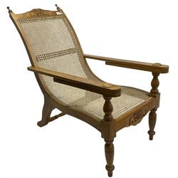 Late 20th century teak framed plantation chair, cresting rail and apron carved with two elephants with upraised trunks, flanked by finials, cane back and seat, fitted with hinged extending leg rests, on ring turned supports