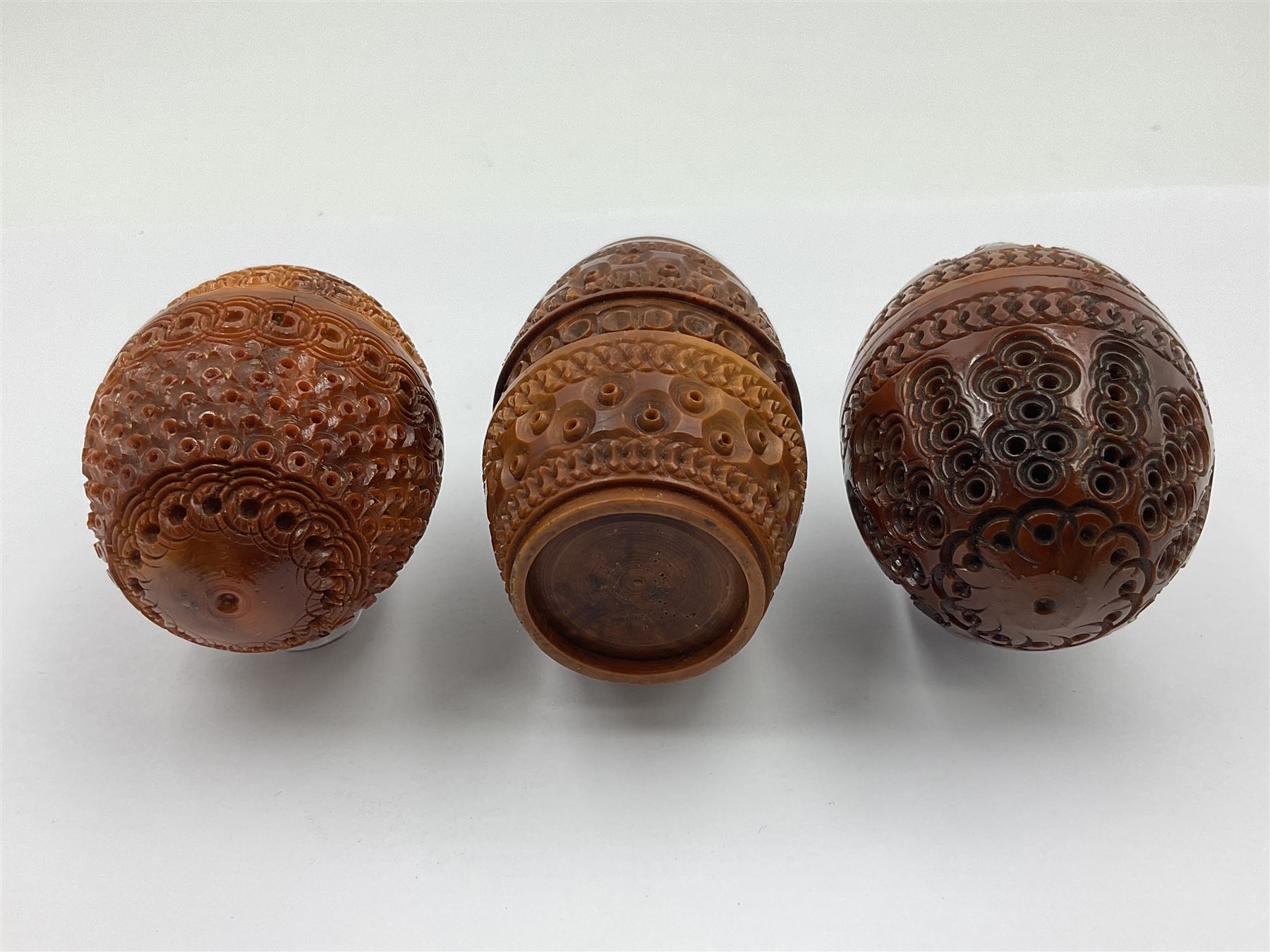 Three 19th century coquilla nut pomanders or flea catchers, two of egg shaped form and the third of barrel from with carved and pierced decoration and screw threaded join, largest H8cm