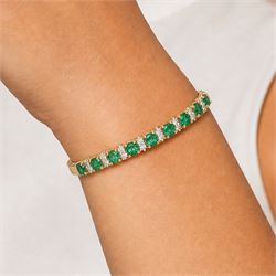 14ct gold emerald and diamond hinged bangle, nine oval cut emeralds, each spaced by two round brilliant cut diamonds, stamped 585, total emerald weight approx  2.15 carat, total diamond weight approx 0.50 carat