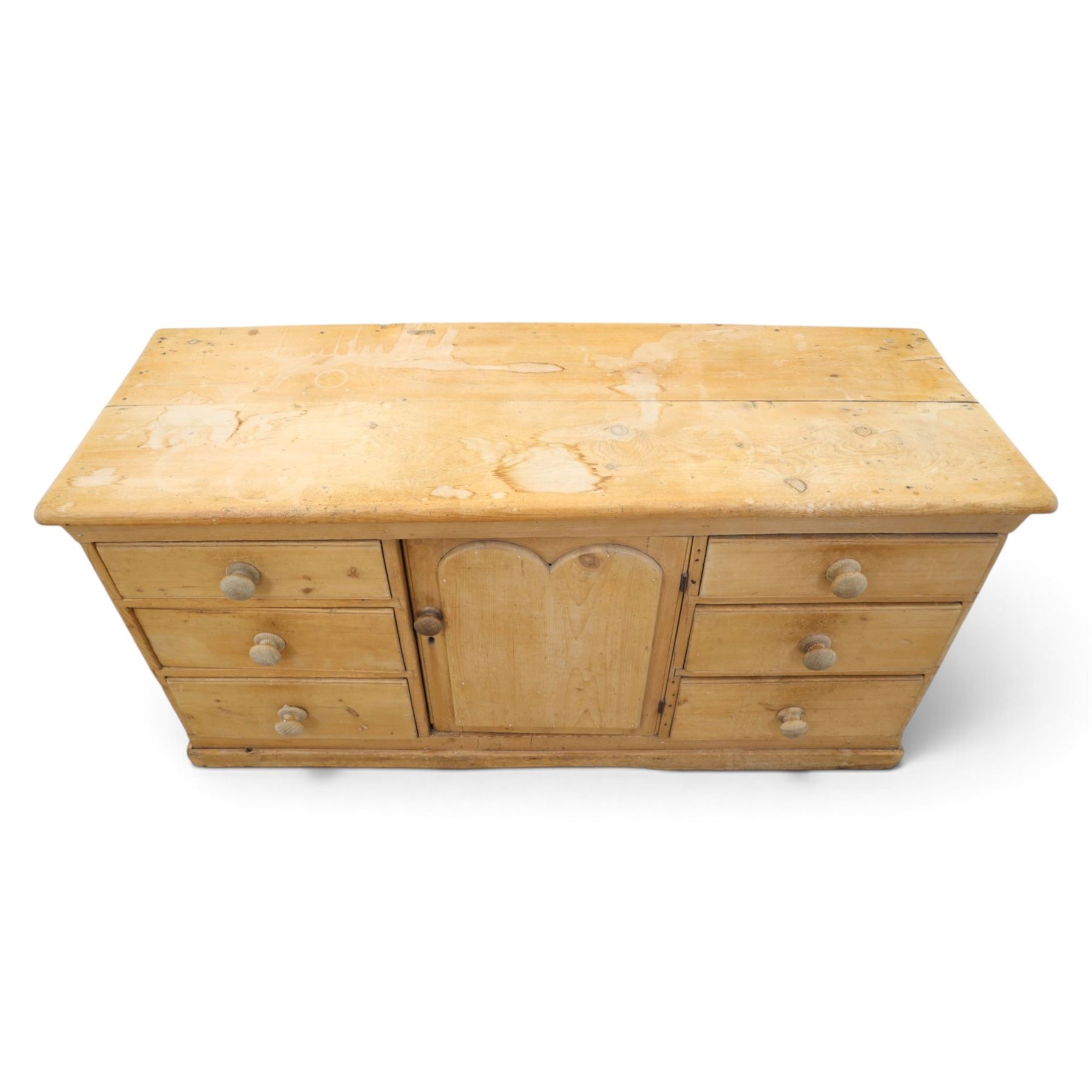 Victorian stripped pine sideboard, rectangular plank top rounded edges, with central cupboard door with shaped panel, flanked by two banks of three graduating drawers with turned knobs, raised on a plinth base 