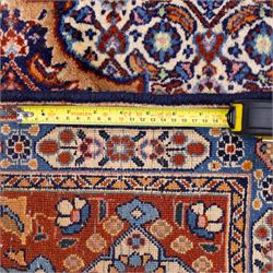 North Eastern Persian Moud hand-knotted carpet, field with central lobbed medallion with radiating serrated palmettes and spandrels in a densely worked all-over ground of small floral rosettes and geometric blossoms within a wide floral border flanked by multiple guard borders in a palette of indigo blue, ivory, terracotta, turquoise, and muted gold, with cotton fringe ends 