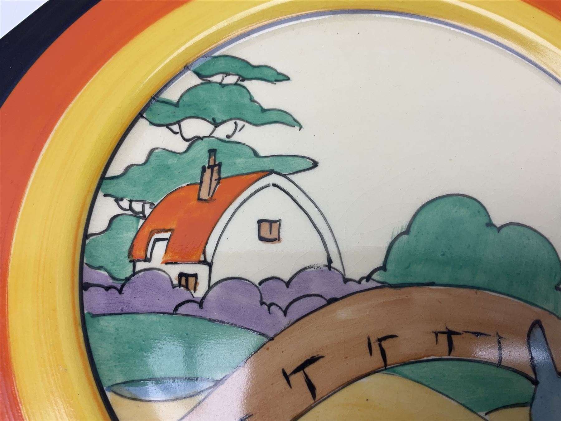 Clarice Cliff Bizarre for Newport Pottery Orange Roof Cottage pattern plate, circa 1932, hand painted with a stylised cottage and bridge landscape with yellow, orange and black banding, black printed mark beneath, D22cm 