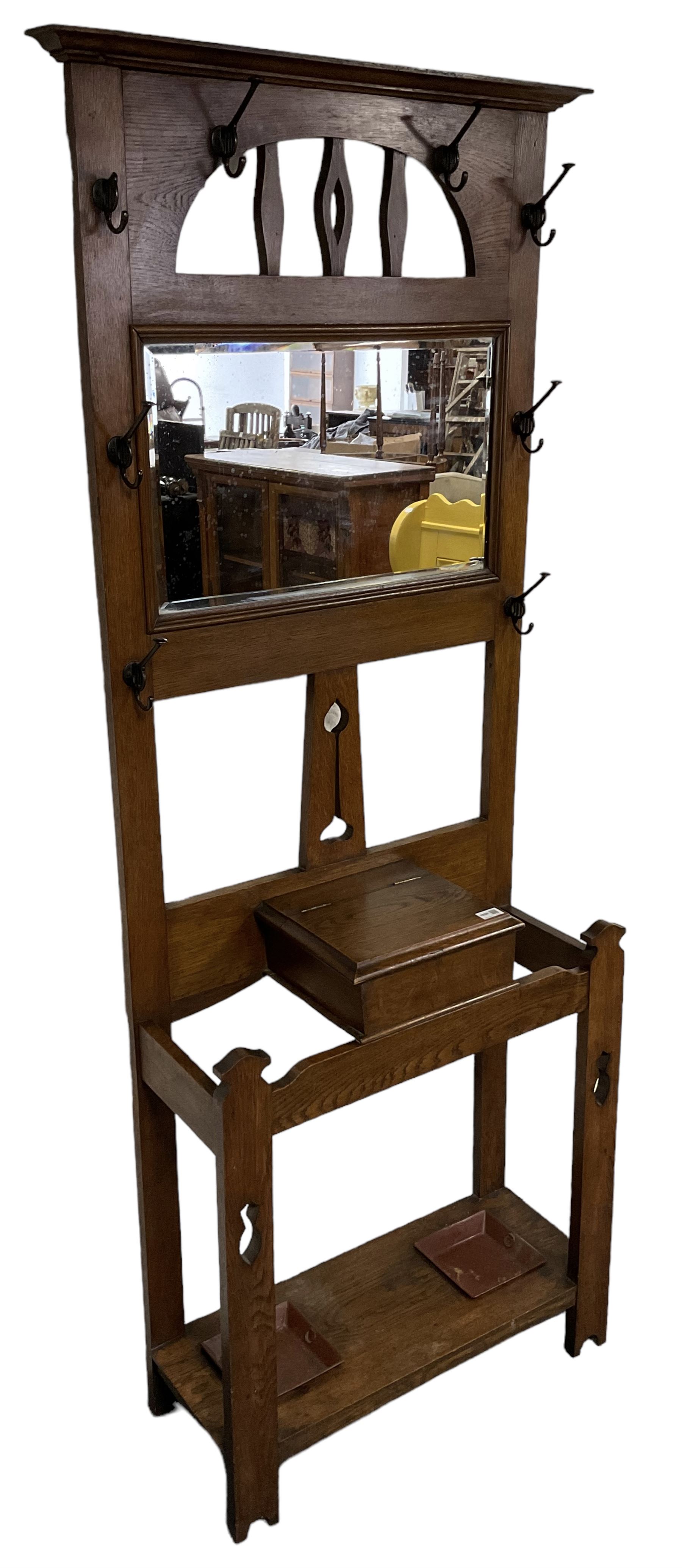 Arts & Crafts period oak hall stand, projecting moulded cornice over arched cut-out decorated with shaped vertical rails, fitted with rectangular bevelled mirror back over hinged glove compartment, on straight pierced supports with shaped pediments 
