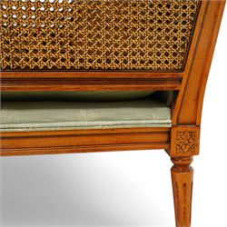 French Empire design varnished wood three piece lounge suite comprising of two cane armchairs and matching sofa, carved top rails with foliate terminals, cane side panels and padded scroll arms, upholstered in a green brocade with matching piping, on fluted legs